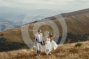 Happy gorgeous bride and groom walking in sun light holding han