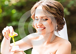 Happy gorgeous bride have fun with bubble blower outdoors in park