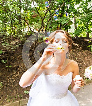 Happy gorgeous bride have fun with bubble blower outdoors in park