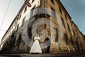 Happy gorgeous bride and stylish groom holding hands and looking