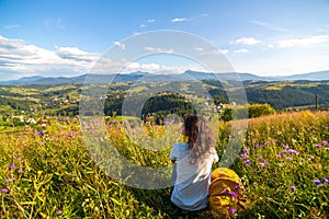 Happy gorgeous girl enjoy hills view sitting in flower field on the hill with breathtaking nature landscape