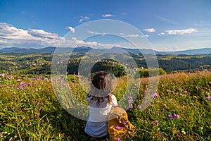 Happy gorgeous girl enjoy hills view sitting in flower field on the hill with breathtaking nature landscape