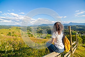 Happy gorgeous girl enjoy hills view sitting in flower field on the hill with breathtaking nature landscape