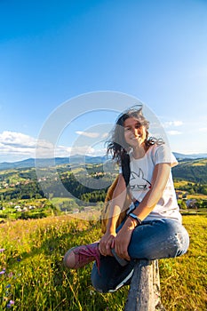 Happy gorgeous girl enjoy hills view sitting in flower field on the hill with breathtaking nature landscape