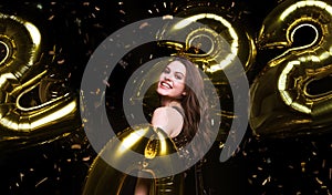 Happy gorgeous girl in stylish sexy party dress holding gold 2022 balloons, having fun at New Year& x27;s Eve Party.