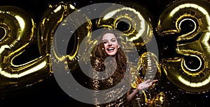 Happy gorgeous girl in stylish sexy party dress holding gold 2023 balloons, having fun at New Year& x27;s Eve Party.