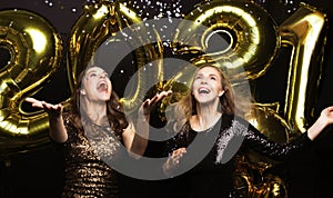 Happy gorgeous girls in stylish sexy party dresses holding gold 2021 balloons, having fun at New Year`s Eve Party