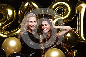 Happy gorgeous girls in stylish sexy party dresses holding gold 2021 balloons, having fun at New Year`s Eve Party