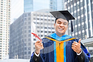 Happy graduate. Happy Asain man in graduation gowns holding diploma in hand on urban city background