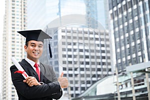 Happy graduate. Happy Asain man in graduation gowns holding diploma in hand on urban city background