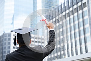 Happy graduate. Happy Asain man in graduation gowns holding diploma in hand on urban city background