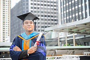 Happy graduate. Happy Asain man in graduation gowns holding diploma in hand on urban city background