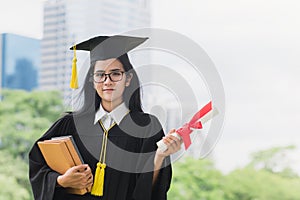 Happy graduate young Asian woman in cap and gown holding a book and certificated in hand, Education concept