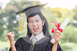 Happy graduate young Asian woman in cap and gown holding certificated in hand, Education concept