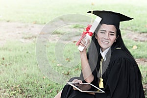 Happy graduate young Asian woman in cap and gown holding certificated and tablet in hand, Education concept