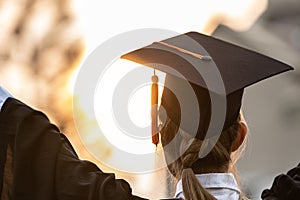 Happy graduated young woman in cap and gown talking with parent in mobile phone and looking certificated in hand so proud