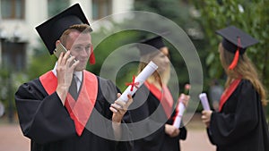 Happy graduation day, student in gown holding smartphone, receiving greetings