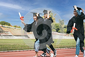 Happy graduation students  holding diploma and running on the stadium at school