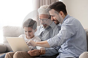 Happy grandfather and father teaching little boy to use laptop