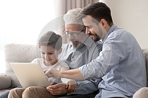 Happy grandfather and father teaching little boy to use laptop photo