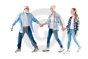 Happy grandfather, grandmother and granddaughter walking and holding hands together