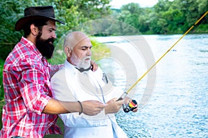 Happy grandfather and grandson with fishing rods on river berth. Angler. Grandfather and boy fishing together. Young man