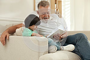 Happy grandfather with his grandson reading book together at home