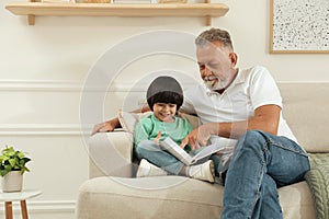 Happy grandfather with his grandson reading book together at home