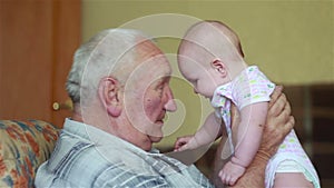 Happy grandfather holds a baby on hands and talking