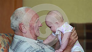 Happy grandfather holds a baby on hands and talking