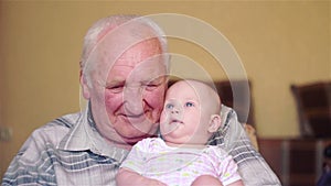 Happy grandfather holds a baby on hands and talking