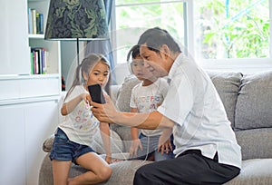 happy Grandfather with kids using smartphone Sharing headphone together for listening to music and enjoying ,dancing on sofa or