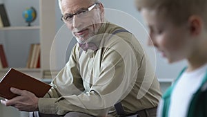 Happy grandfather looking with love at grandson reading book, feeling proud