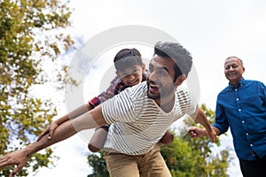 Happy grandfather looking at man giving piggy backing to son