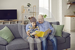 Happy grandfather reading book to his grandson while sitting on sofa in the living-room