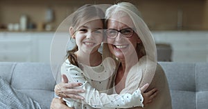 Happy grandma and sweet granddaughter child hugging on home couch