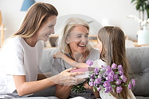 Happy grandma thanking grandchild and grown daughter for flowers