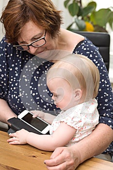 Happy grandmother and cute granddaughter using smartphone, teaching