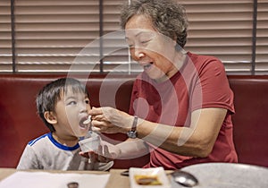 Happy grandmother feeds her grandson in restaurant