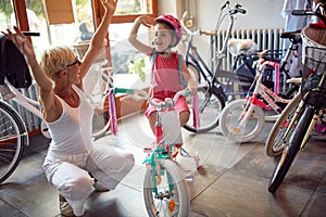 Happy grandmother and girl buying bicycle and helmets in bike shop