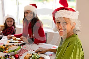 Happy grandmother, granddaughter and adult daughter wearing santa hats sitting at christmas table