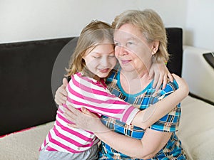 Happy grandmother and granddaughter hugging at home on the couch