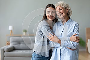 Happy grandmother and granddaughter hugging, standing in living room