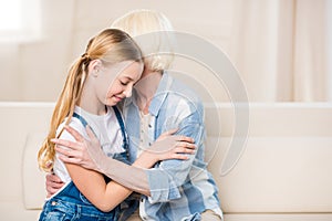 Happy grandmother and granddaughter sitting on sofa and hugging