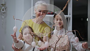 Happy grandmother and granddaughters admiring painted eggs talking smiling. Front view portrait of Caucasian woman and