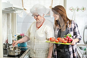 Happy grandmother and her granddaughter cooking together at kitchen.