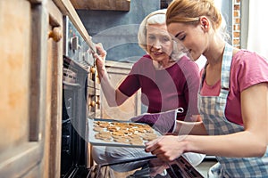 Happy grandmother and her teenage granddaughter removing Christmas cookies from