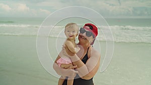 Happy grandmother holding her little baby grandchild at the beach with the ocean in the background
