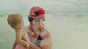 Happy grandmother holding her little baby grandchild at the beach with the ocean in the background