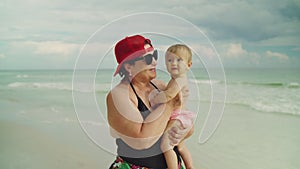 Happy grandmother holding her little baby grandchild at the beach with the ocean in the background